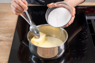 Zucker zur Butter und Sahne in den Topf geben