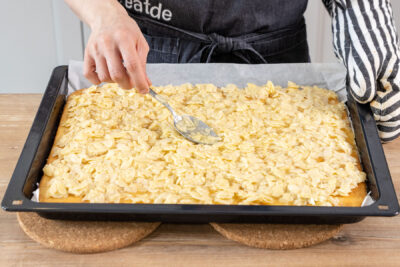 Mandelschicht auf dem vorgebackenen Boden für den Mandelkuchen vom Blech verstreichen