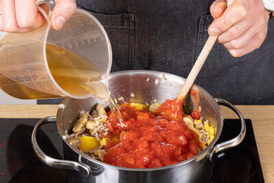 Gemüsebrühe und gehackte Tomaten mit in den Topf geben