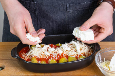 Emmentaler und Feta über die vegetarischen Cannelloni streuen