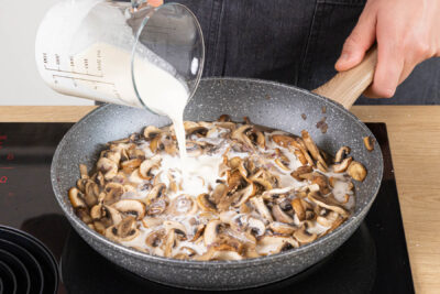 Weißwein, Sahne und Gemüsebrühe zu den Champignons geben