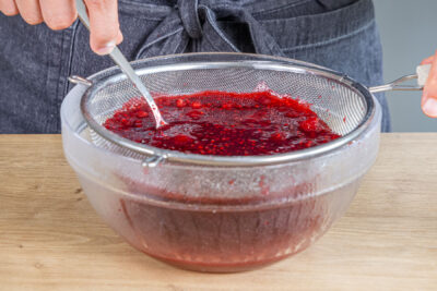 Himbeermarmelade aus gefrorenen Himbeeren durch ein Sieb streichen