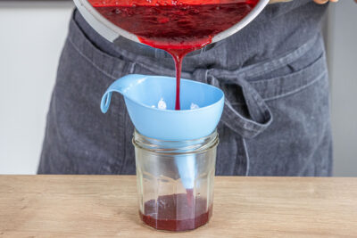 Himbeermarmelade aus gefrorenen Himbeeren durch einen Trichter in Gläser füllen