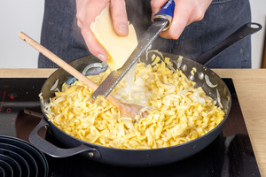 Käse über die Spätzle in der Pfanne reiben
