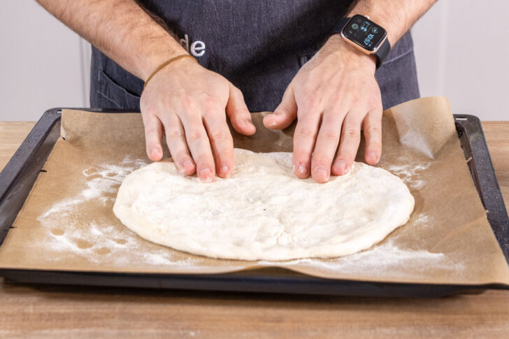 Neapolitanischer Pizzateig auf dem Blech rund auseinanderziehen