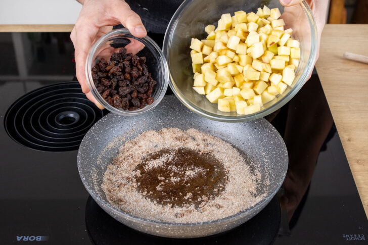 Apfelstücke und Rosinen zum Zucker in die Pfanne geben