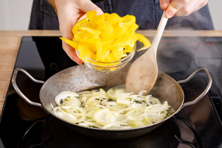 Paprikastreifen zur Zwiebel in die Pfanne geben
