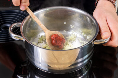 Tomatenmark zu dem Knoblauch und den Zwiebelwürfeln in den Topf geben