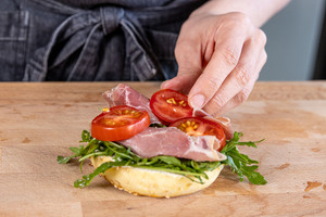 Toamtenscheiben auf den Rucola mit Schinken geben