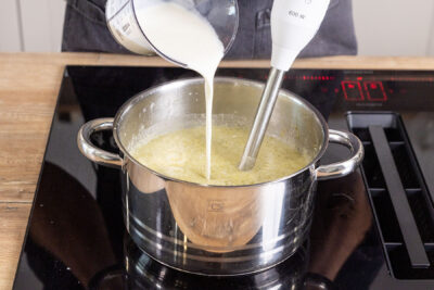 Sahne zur Blumenkohl-Brokkoli-Suppe gießen