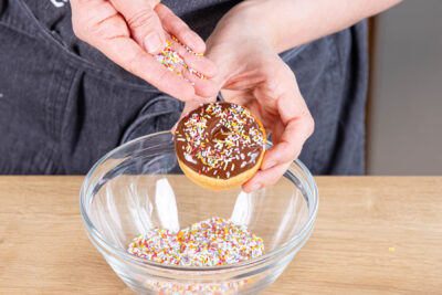 Donuts aus dem Backofen mit Schokoglasur und Zuckerstreusel verzieren