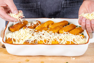 Käse über dem Fischstäbchenauflauf verteilen