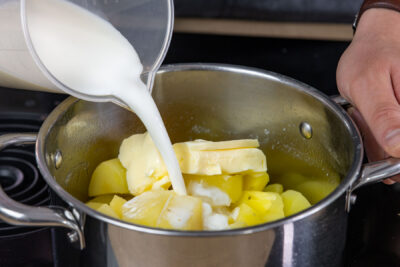 Milch und Butter zu den Kartoffeln geben