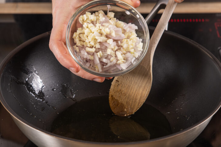 Knoblauch und Zwiebeln in die Pfanne geben