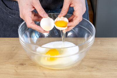 Für die Quarkmasse der Eierschecke Eier zum Zucker geben