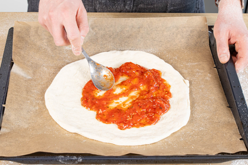 Tomatensauce auf dem Pizzaboden verstreichen