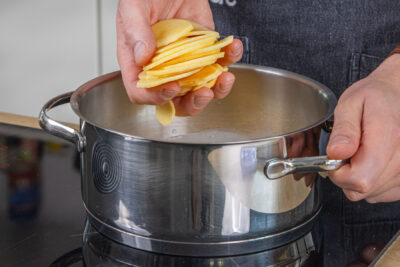 Kartoffelscheiben in den Topf geben