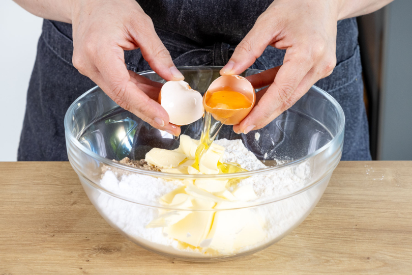 Ei zum Mehl und den restlichen Zutaten des Mürbeteigs geben