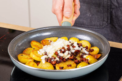 Zwiebelwürfel und Schinkenwürfel mit zu den Bratkartoffeln geben