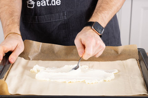 Den Blätterteig mit Frischkäse bestreichen.