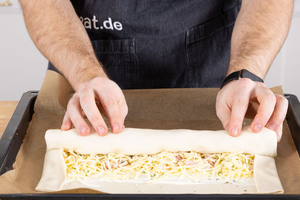 Den Blätterteigstrudel mit Schinken und Käse von unter her aufrollen.
