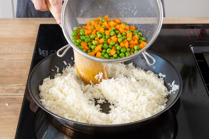 Erbsen und Karotten zum Reis in die Pfanne geben