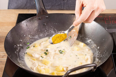 Hähnchen-Ananas-Cury mit Chiliflocken und Curry würzen