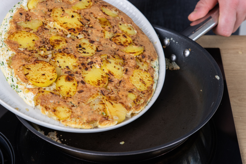 Omelett mit Kartoffeln vom Teller in die Pfanne gleiten lassen