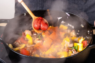 Tomatenmark, Currypulver und Paprikapulver in den Bräter geben