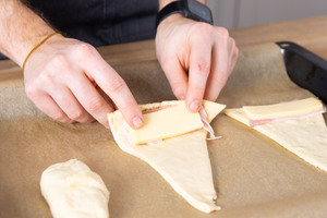 Schinken-Käse-Croissantteig von unten her aufrollen.
