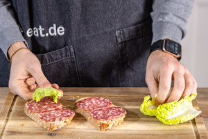 Brotscheiben mit Salami und Salat belegen