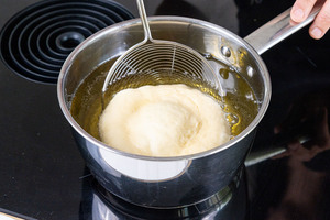 ausgezogenen Krapfen ins heiße Fett in den Topf geben