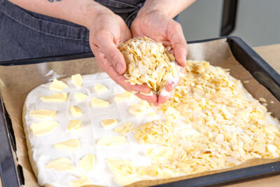 Mandelblättchen und Zucker über Omas Butterkuchen streuen