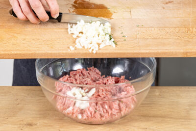 Zwiebel und Rosmarin zum Hackfleisch geben