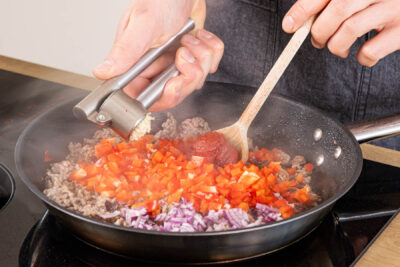 Gemüsewürfel und Tomatenmark zum Hackfleisch geben