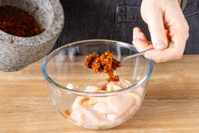 Kräuter im Mörser zerkleinern und Hähnchenfleisch marinieren