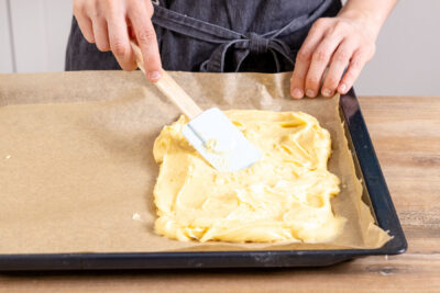 Brandteig für die Karpatka auf dem halben Backblech verstreichen