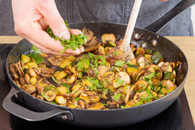 gehackte Petersilie zur Pilz-Zucchini-Pfanne geben