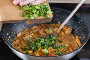 Frühlingszwiebeln zum Hähnchencurry mit Reis und Gemüse geben
