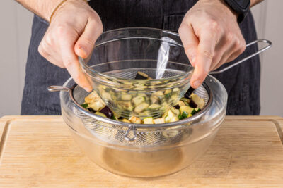 Zucchini- und Auberginewürfel im Sieb beschweren. Abtropfen lassen