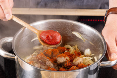Gewürze, Mehl und TOmatenmark zum Fleisch geben