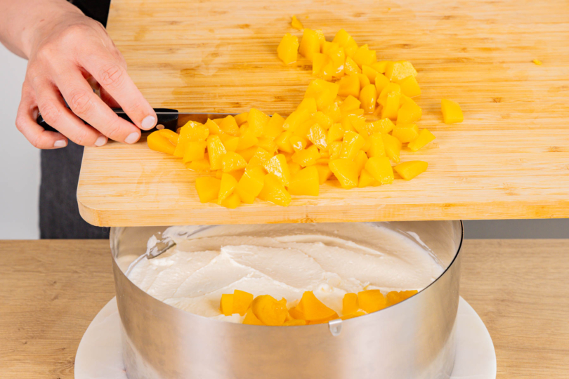 Hälfte der Joghurtcreme auf Tortenboden verstreichen und gewürfelte Pfirsiche darauf verteilen