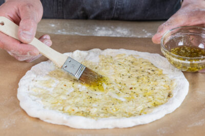 Kräuter-Öl auf der Pizza verteilen
