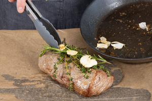 Die Kräuter, den Knoblauch und das Bratöl auf dem gebratenen Rinderfilet verteilen.