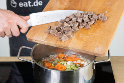 Gemüse und Fleisch in den Topf geben
