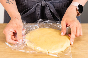 Mürbeteig platt drücken und mit Frischhaltefolie umwickeln