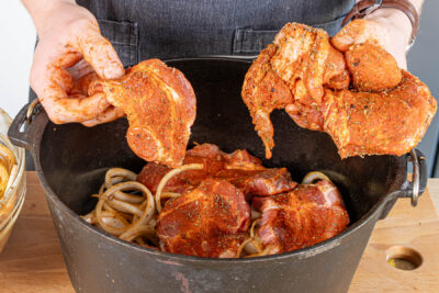 mariniertes Fleisch und Zwiebeln in den Dutch Oven schichten