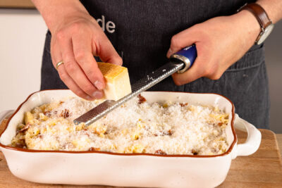 restlichen Parmesan über den Carbonara-Auflauf reiben