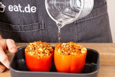 Gefüllte Paprika in eine Auflaufform geben und Wasser angießen