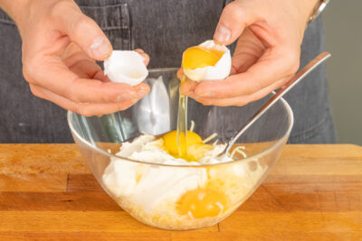 Eier in Schüssel mit Crème fraîche und geriebenen Emmentaler geben